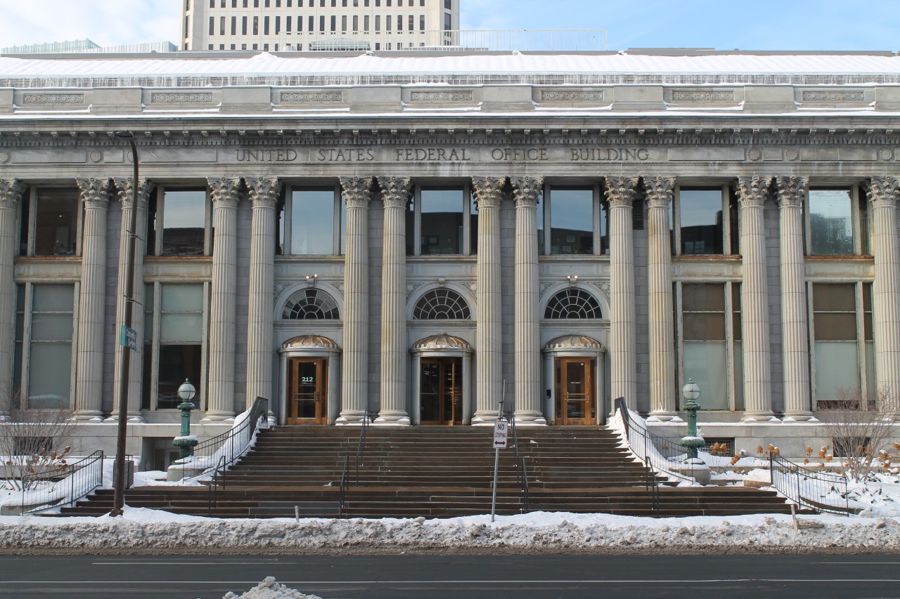 Exterior of the Minneapolis Passport Agency. It is a grey stone building with columns between each door and window.