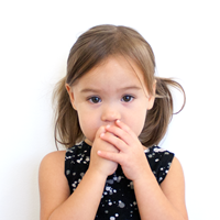 Foto de una niña pequeña cubriéndose la boca con la mano. 